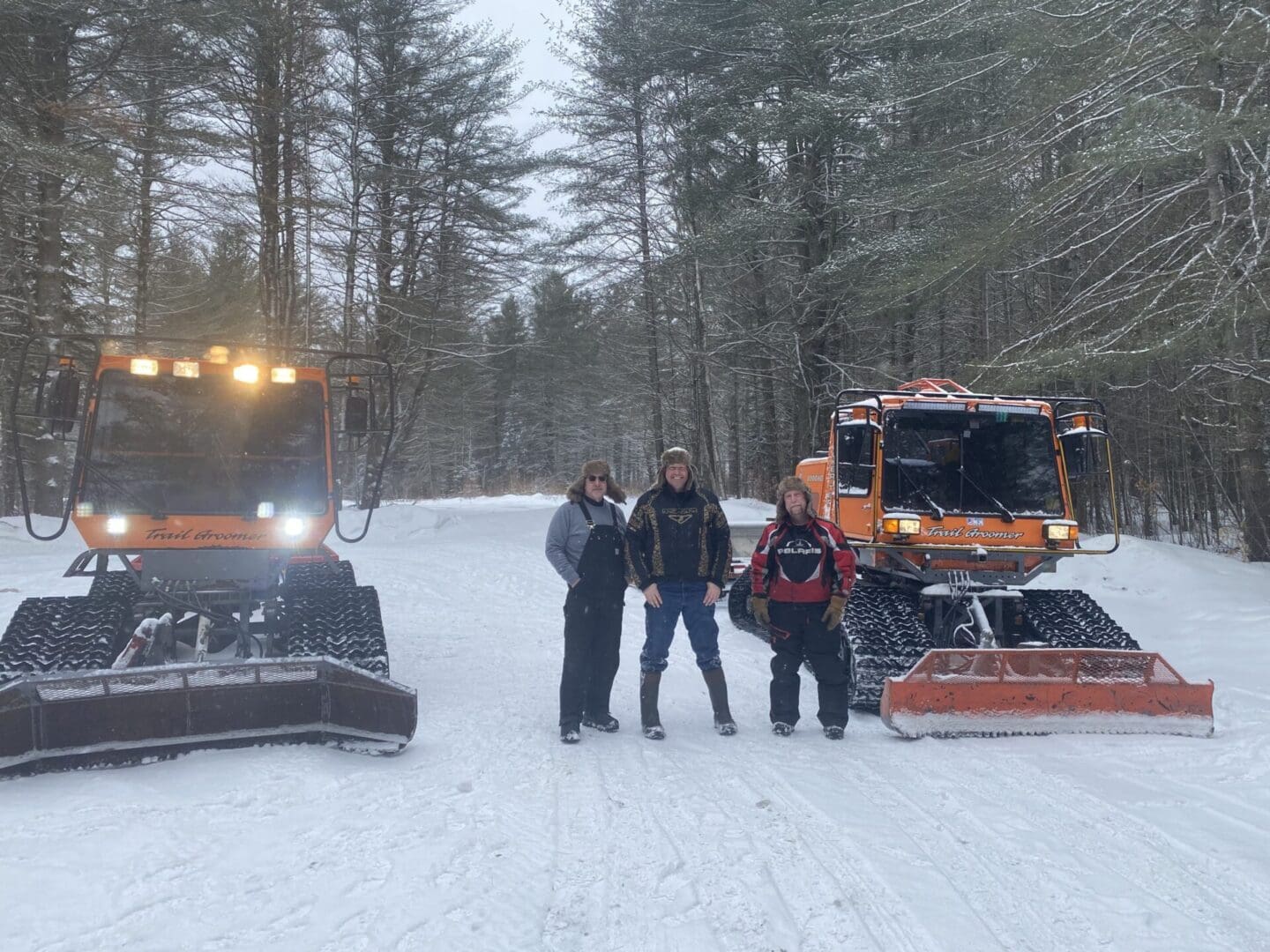 Three people standing in front of a snow plow.