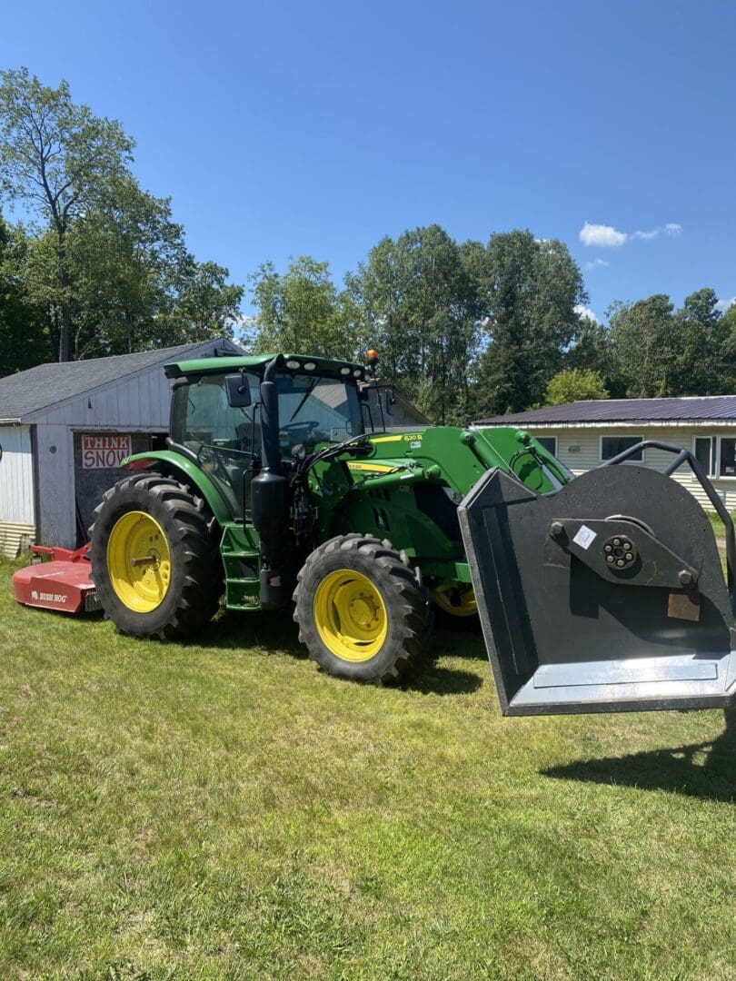 A tractor is parked in the grass near a shed.