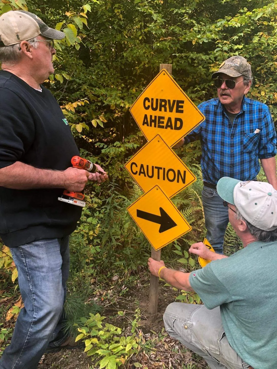 Three men are holding a sign that says " curve ahead caution ".